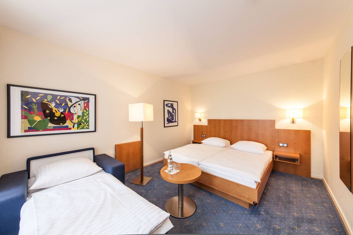 A hotel room with two beds, a small table, and two bedside lamps.
