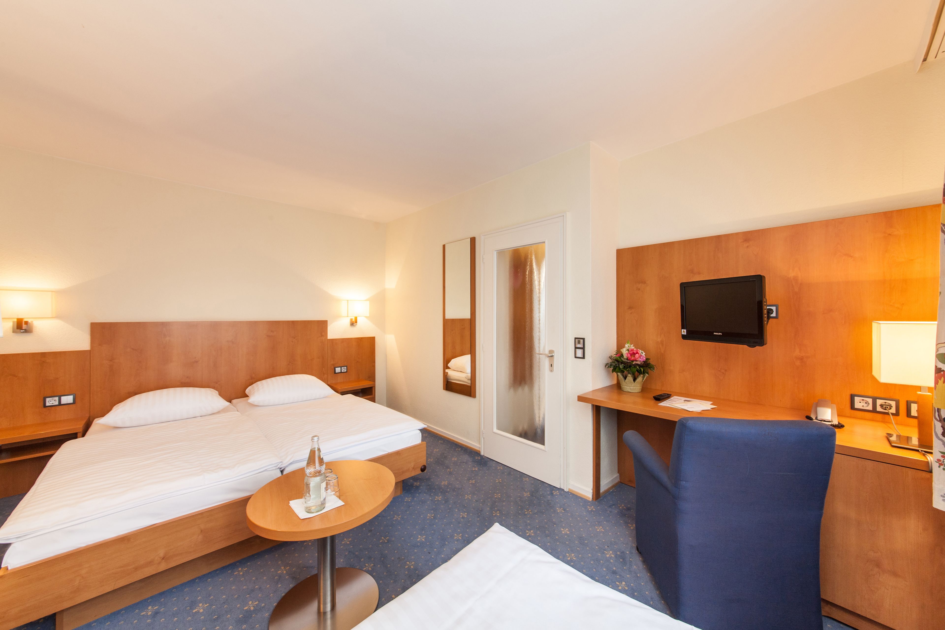 Habitación de hotel con una cama, un escritorio, una silla, una mesita y un televisor.
