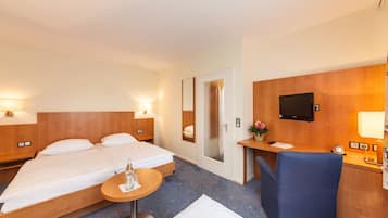 Habitación de hotel con una cama, un escritorio, una silla, una mesita y un televisor.