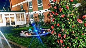 A garden with a fountain and a rose bush in front of a building with multiple windows. - Hotel Drei Kronen Elmshorn (Elmshorn)