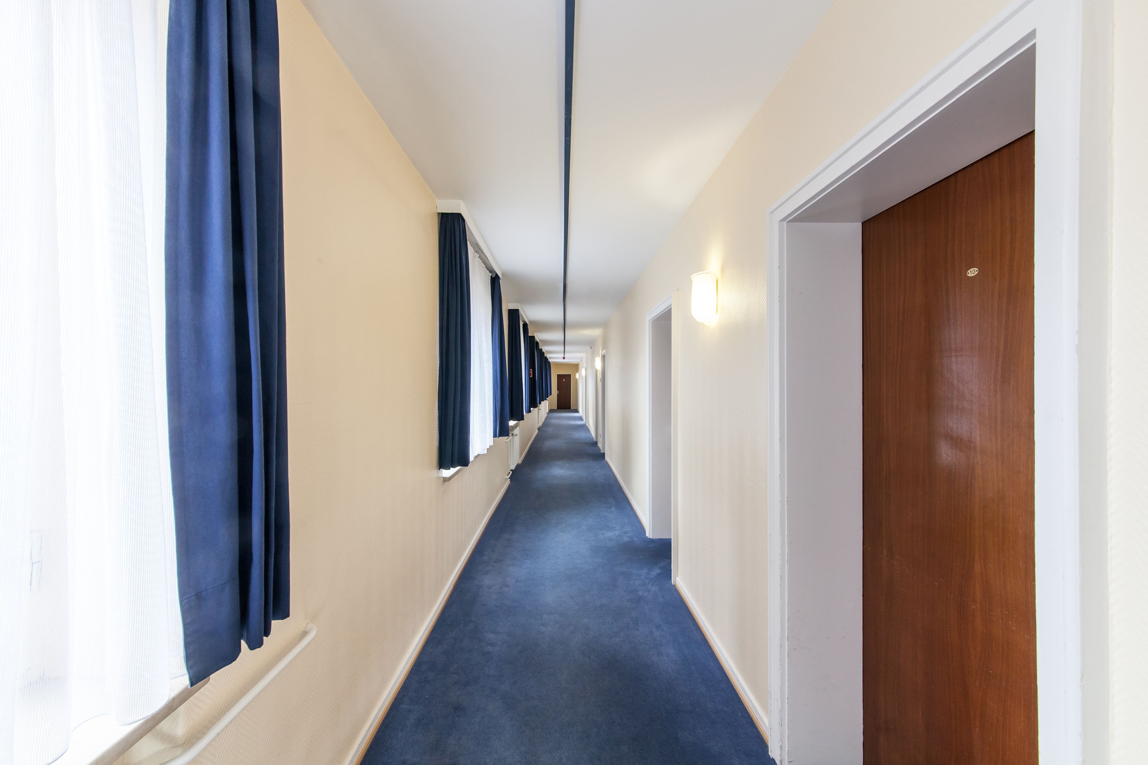 A long, narrow hallway with a blue carpet, white walls, and a wooden door at the end.