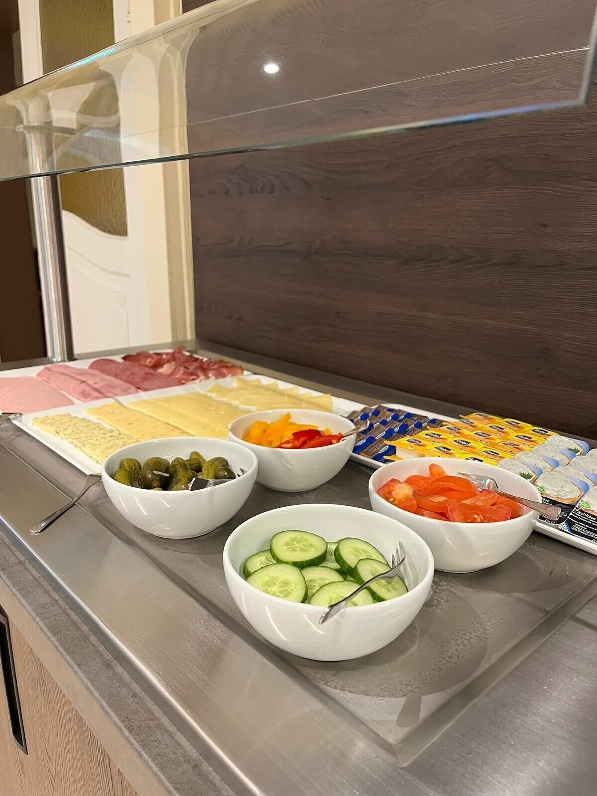 A buffet with various food items including sliced cucumbers, olives, and different types of cheese.