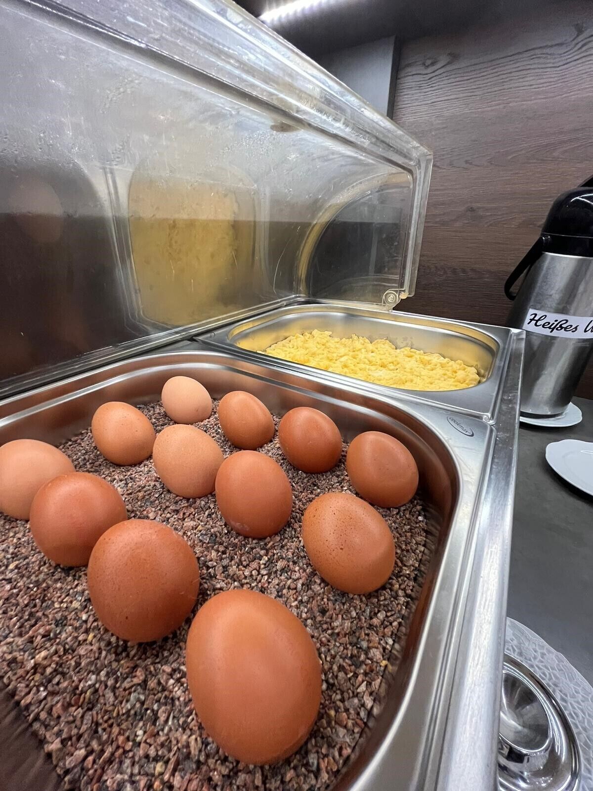 Zona de bufé con un recipiente de huevos revueltos y una bandeja de huevos marrones sobre una base de arroz.