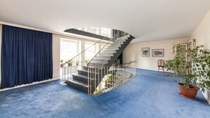 A spacious room with a blue carpet, a spiral staircase, a potted plant, and framed pictures on the wall. - Hotel Drei Kronen Elmshorn (Elmshorn)