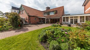 A courtyard with a brick building, a covered patio, and a garden with various plants and flowers. - Hotel Drei Kronen Elmshorn (Elmshorn)