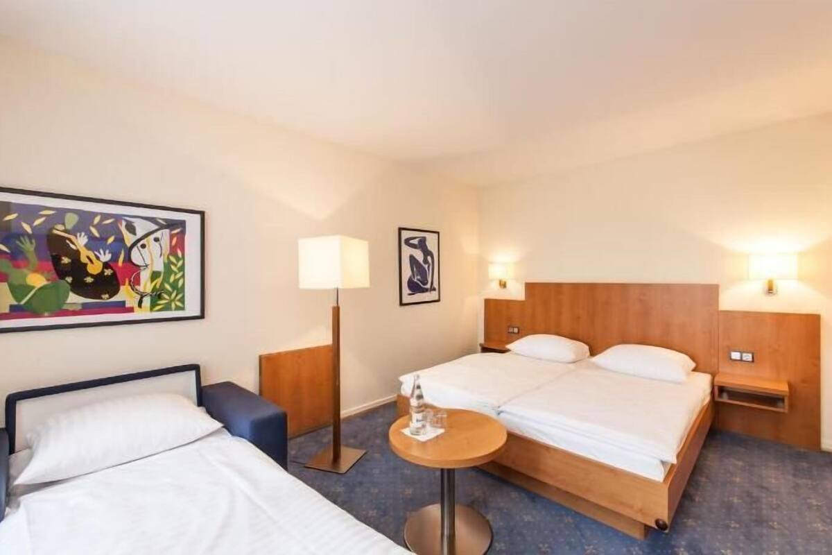 A hotel room with two beds, a desk, a chair, a lamp, and artwork on the walls.