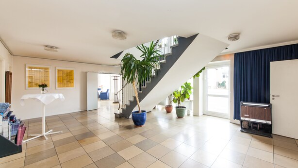 A spacious living area with a modern staircase, potted plants, and a flat-screen TV. - Hotel Drei Kronen Elmshorn (Elmshorn)