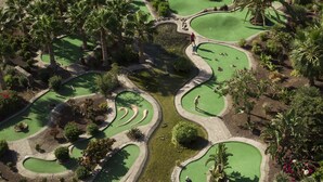 Un parcours de golf avec plusieurs greens, des palmiers et une plage en arrière-plan.