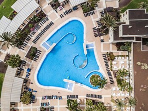 Luchtbeeld van een hotel met een groot zwembad, ligbedden en palmbomen.