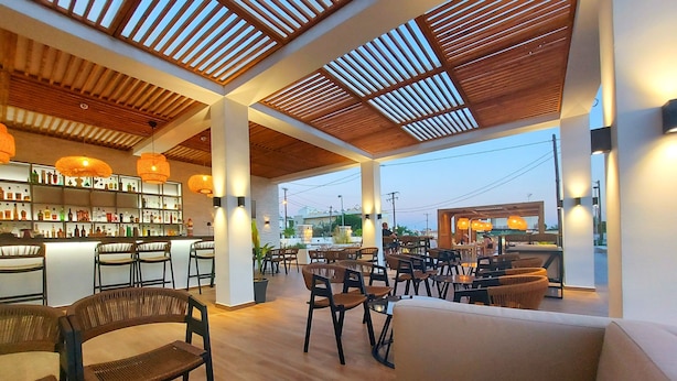 A spacious indoor area with wooden ceiling slats, seating arrangements, and a bar area with shelves of bottles. - Sunshine Hotel Lardos (Rhodes)