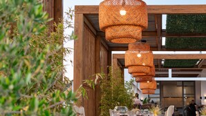 An outdoor dining area with a wooden pergola, hanging wicker lamps, and a table set for two. - Sunshine Hotel Lardos (Rhodes)