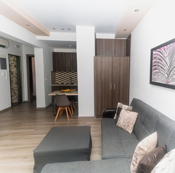 Una sala de estar moderna con un sofá gris, una mesa de comedor con sillas, y una cocina con armarios de madera.
