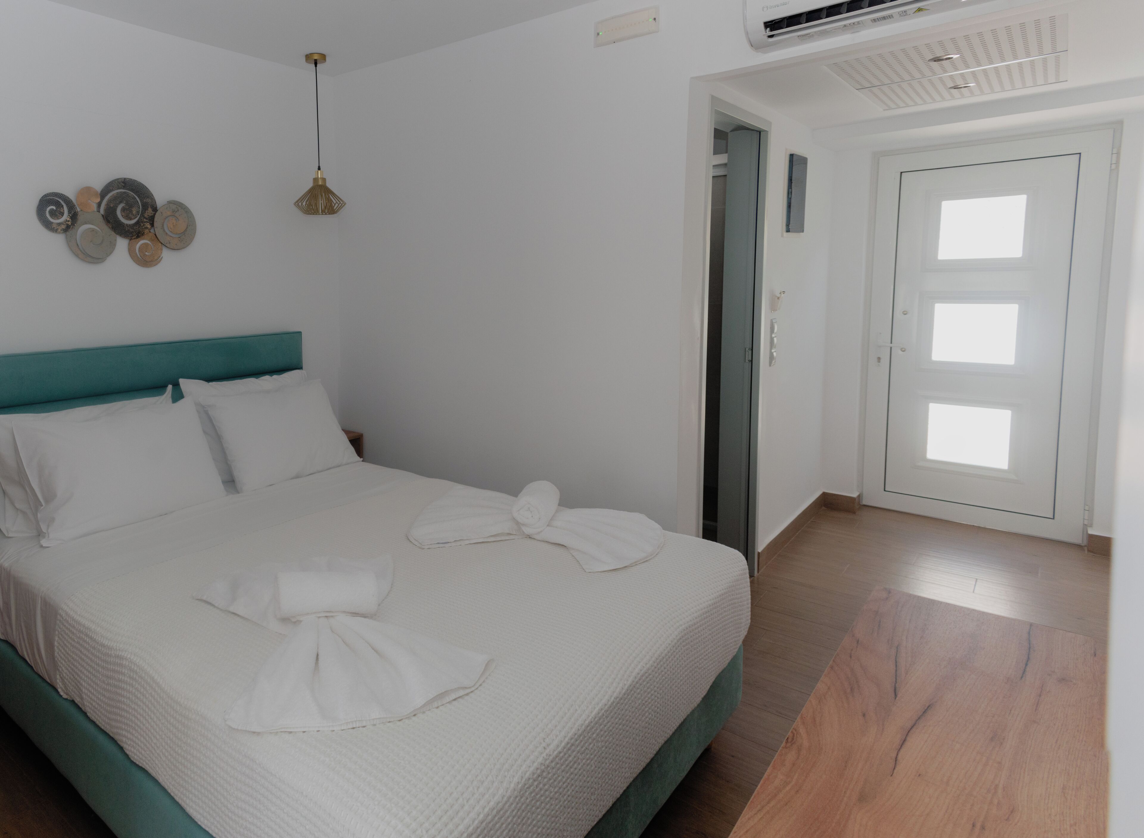 A neatly made bed with white linens and towels, a teal headboard, and a wall-mounted air conditioning unit.