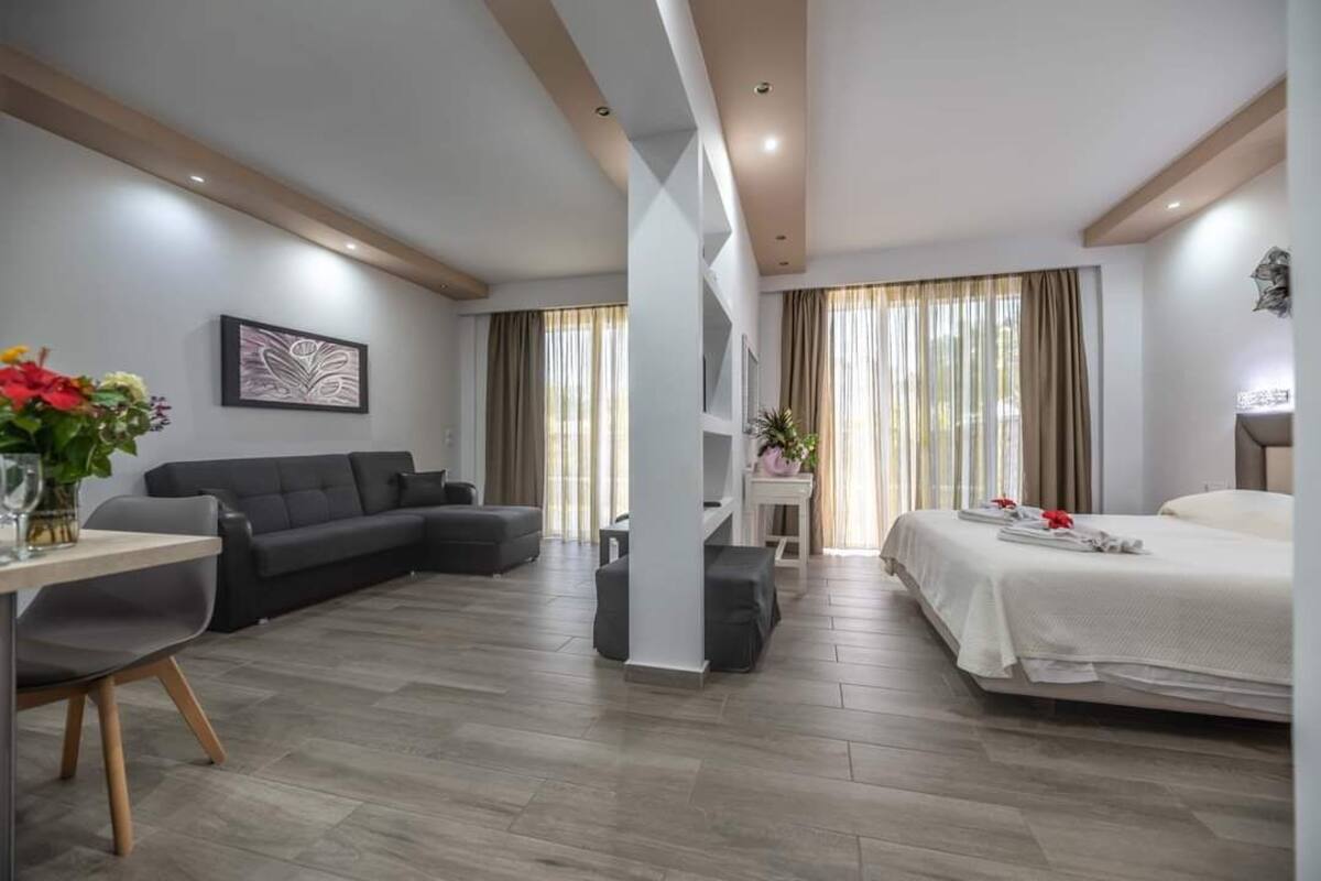 A modern hotel room with a sofa, a bed, a dining table, and a small table with a vase of flowers.