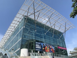 A modern glass building with a large billboard advertising an event.