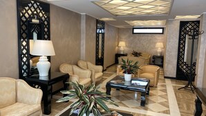 A spacious lobby with a checkered floor, leather armchairs, a coffee table with magazines, and a potted plant.