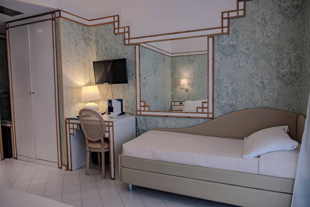 A bedroom with a bed, a desk with a chair, a television, and a mirror.
