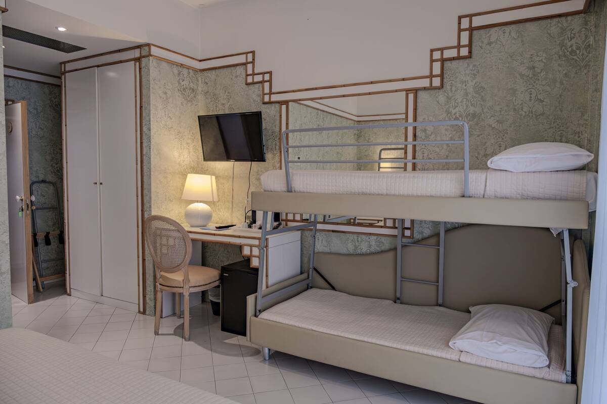 A bunk bed room with a desk, chair, TV, and a small refrigerator.