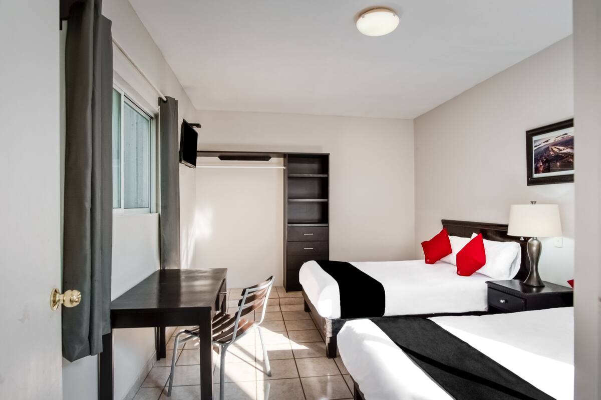 A hotel room with two beds, a desk, a chair, a TV, and a bookshelf.