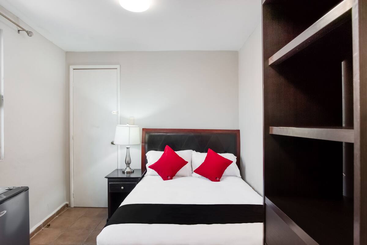 A hotel room with a bed, a nightstand with a lamp, a wardrobe, and a door.
