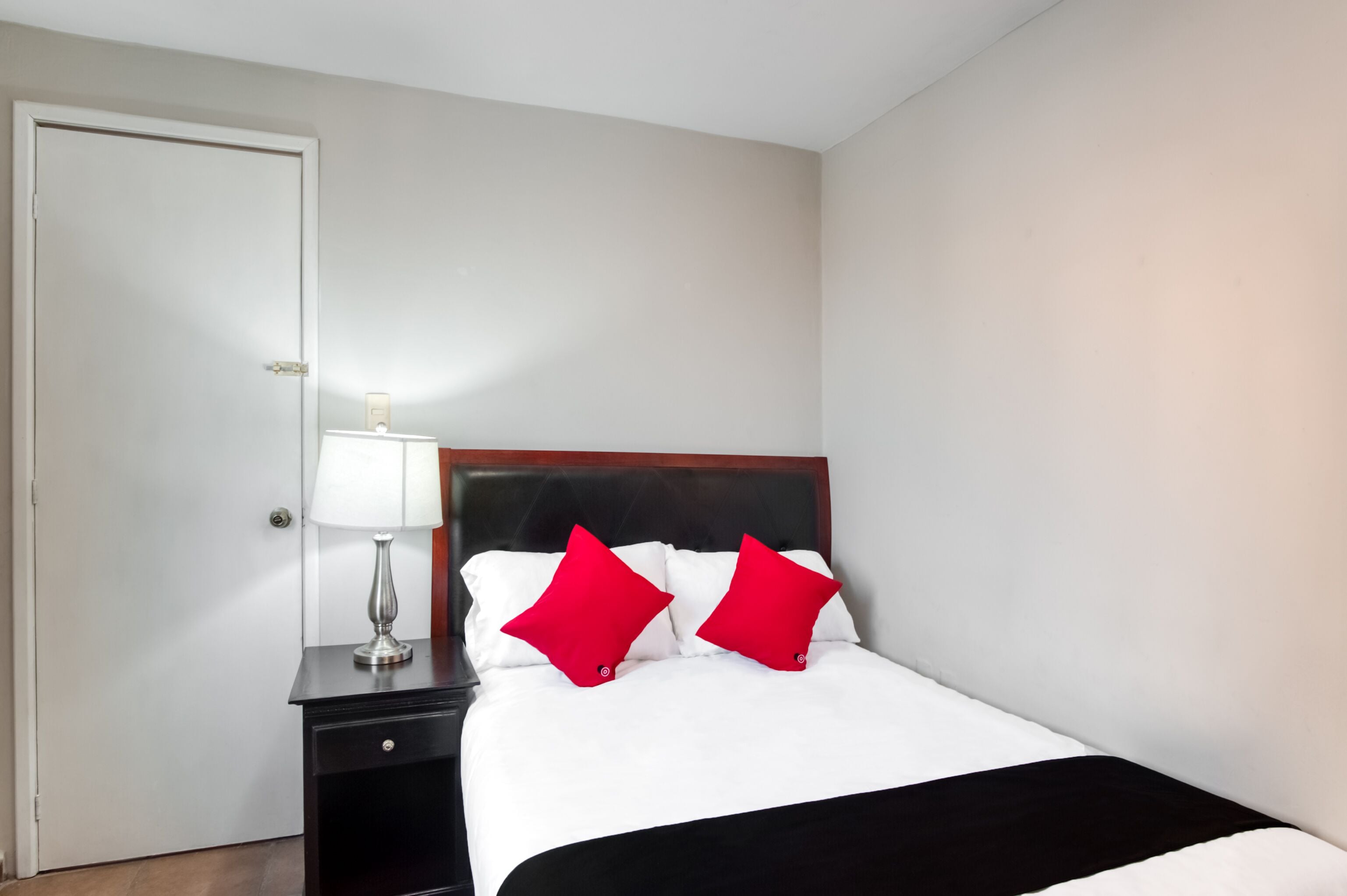 A hotel room with a bed, a nightstand, a lamp, and a door.