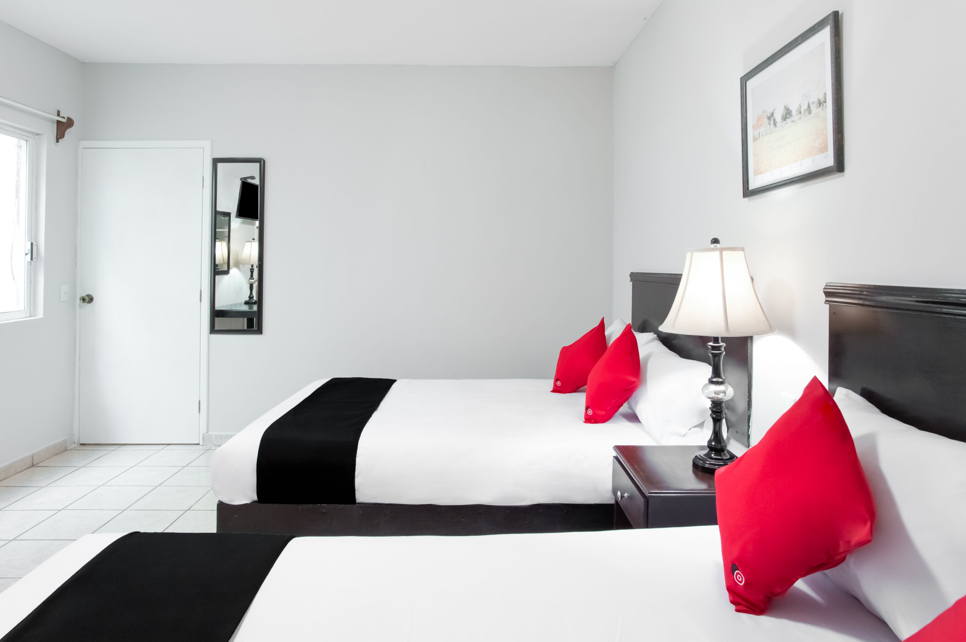 A hotel room with two beds, a nightstand with a lamp, a mirror, and a framed picture on the wall.