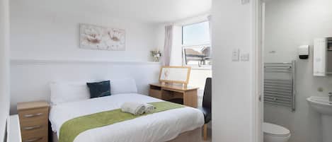 Een hotelkamer met een bed, nachtkastje, spiegel, raam en een badkamer met wastafel en toilet.
