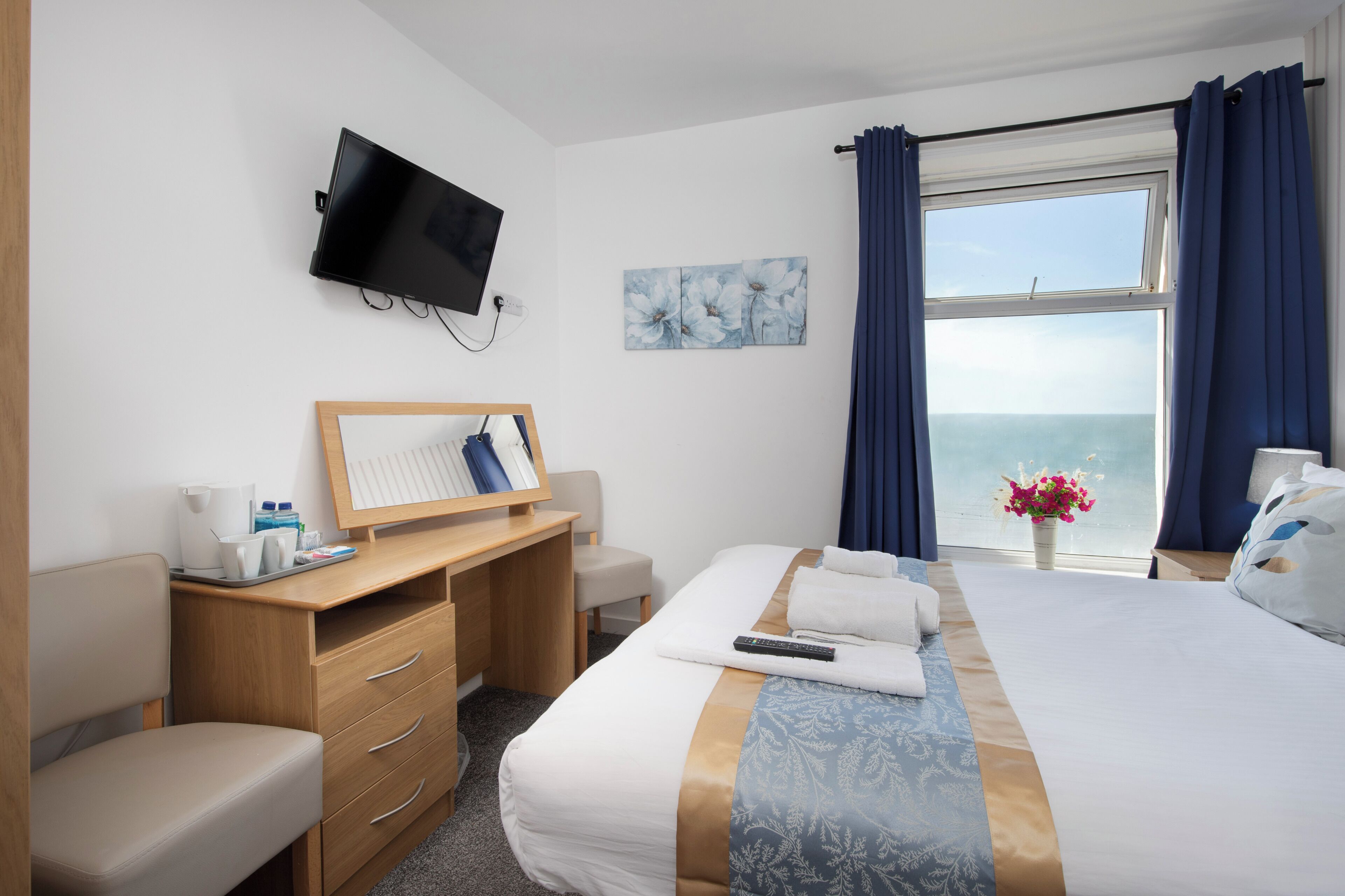 Une chambre d’hôtel avec un lit, un bureau, une chaise, une télévision et une fenêtre avec des rideaux.