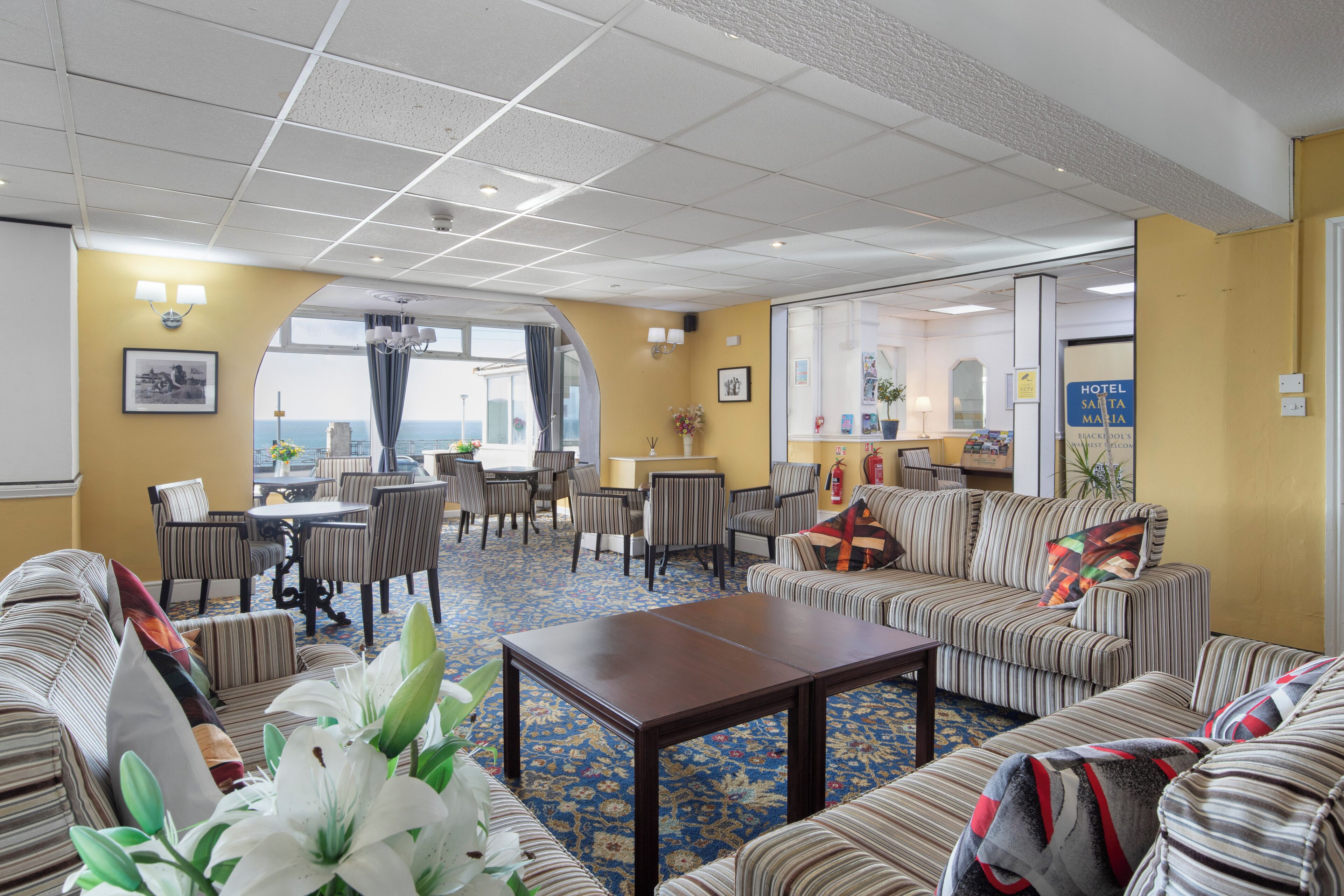 A hotel lobby with striped sofas, a coffee table, a dining area with chairs, and a view through a large window.