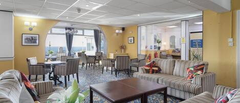 A hotel lobby with striped sofas, a coffee table, a dining area with chairs, and a view through a large window.