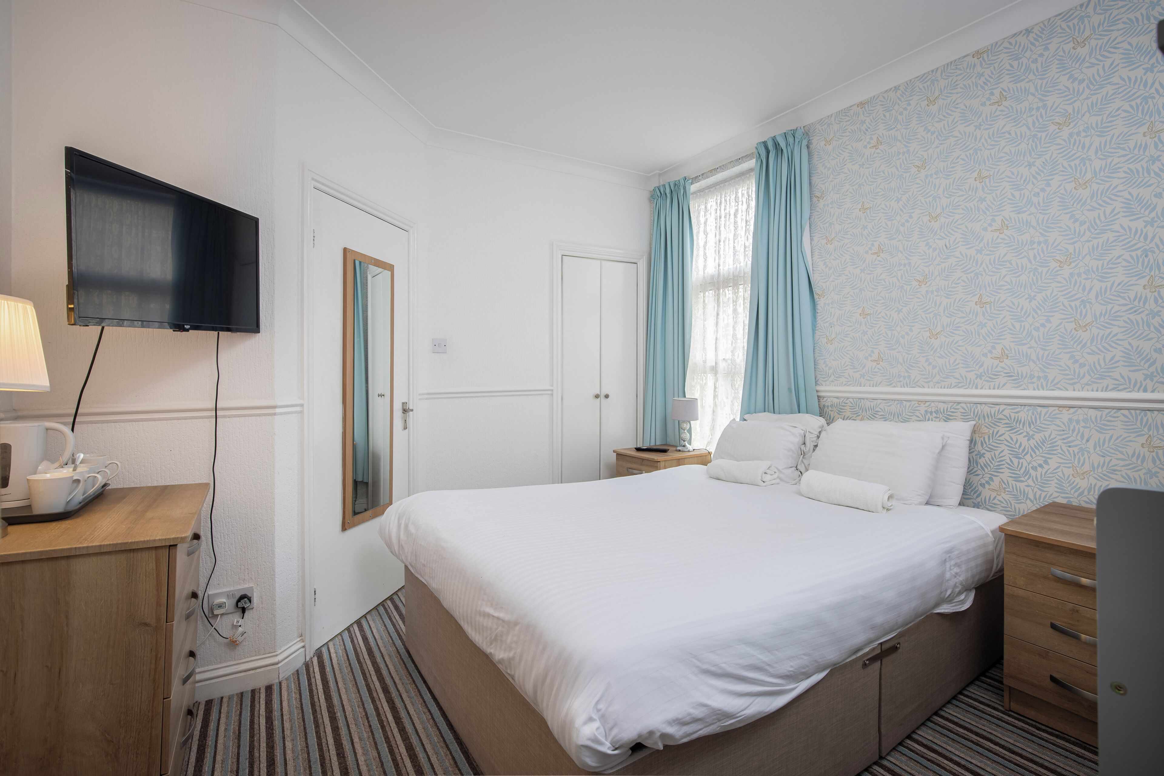 A hotel room with a bed, bedside tables, a TV, and a window with curtains.