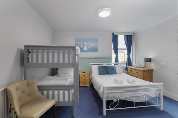A bedroom with bunk beds, a single bed, a bedside table, a chair, and a painting on the wall. - Hotel Santa Maria (Blackpool)