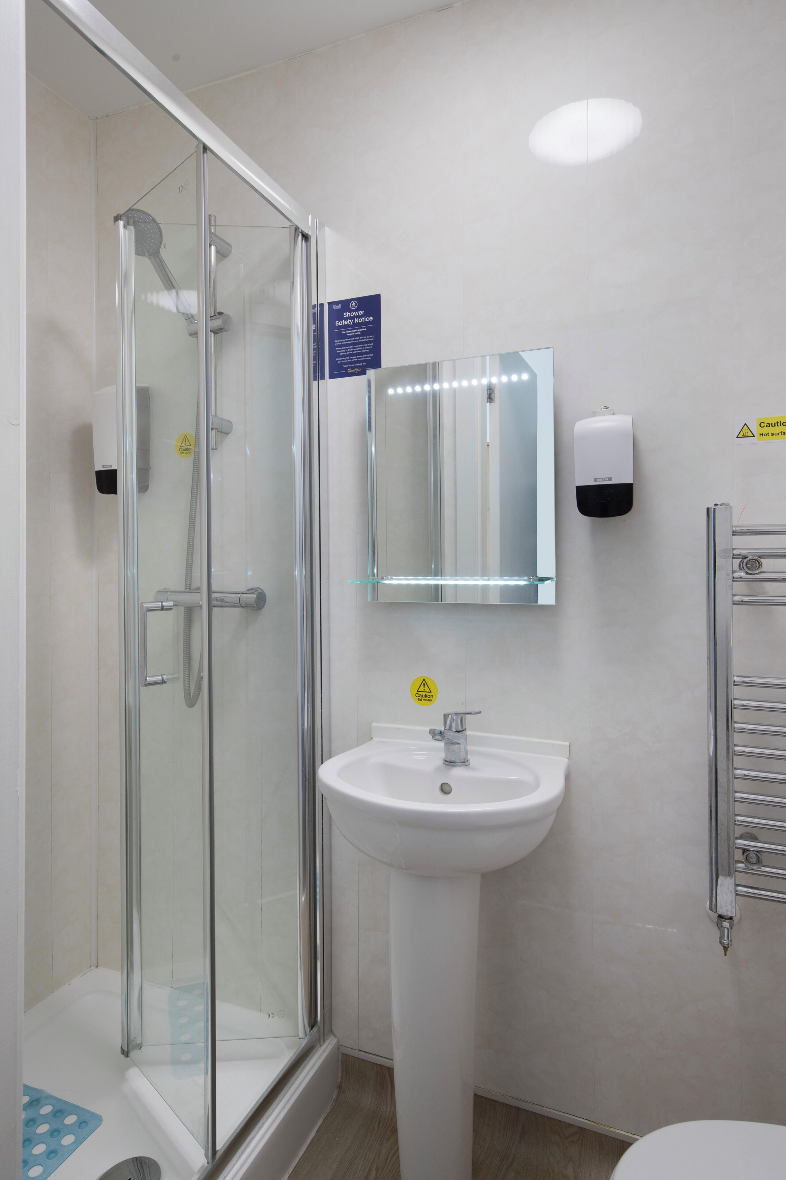 A bathroom with a glass-enclosed shower, a sink, and a mirror with lights.