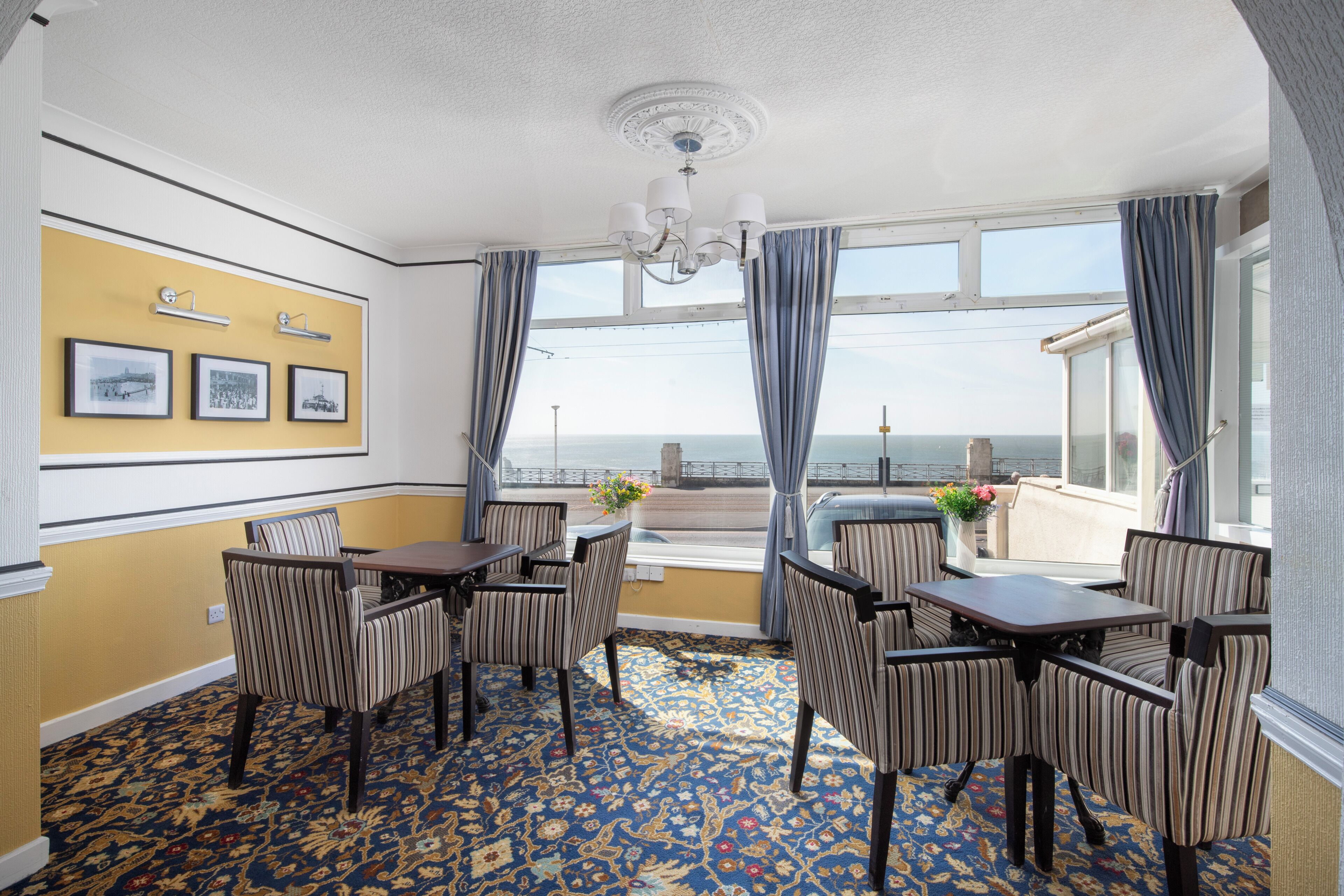 A hotel room with a dining area, a patterned carpet, a view of the sea, and framed pictures on the wall.