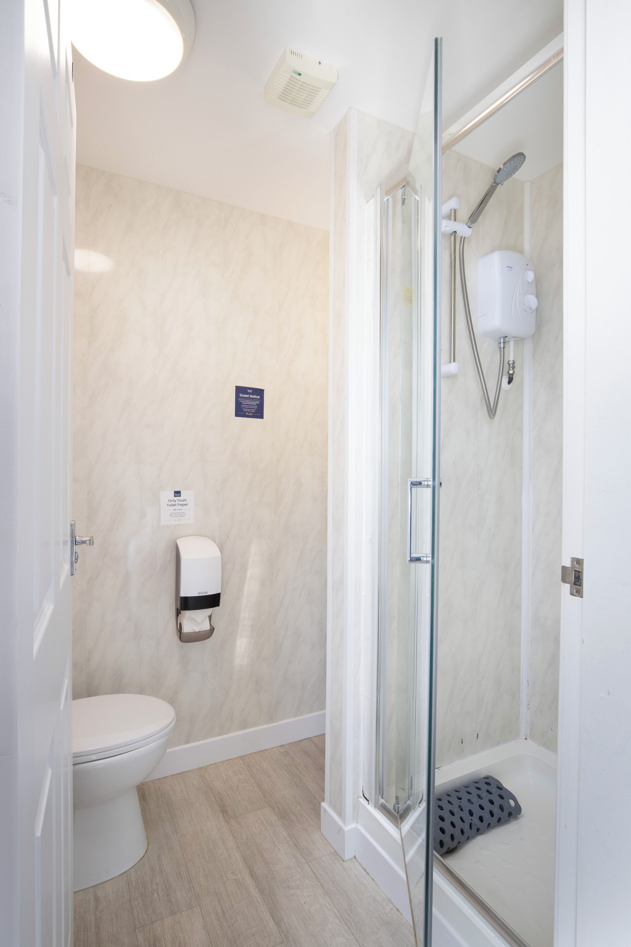 Een moderne badkamer met een douche met glazen wand, een toilet en een papierdispenser.