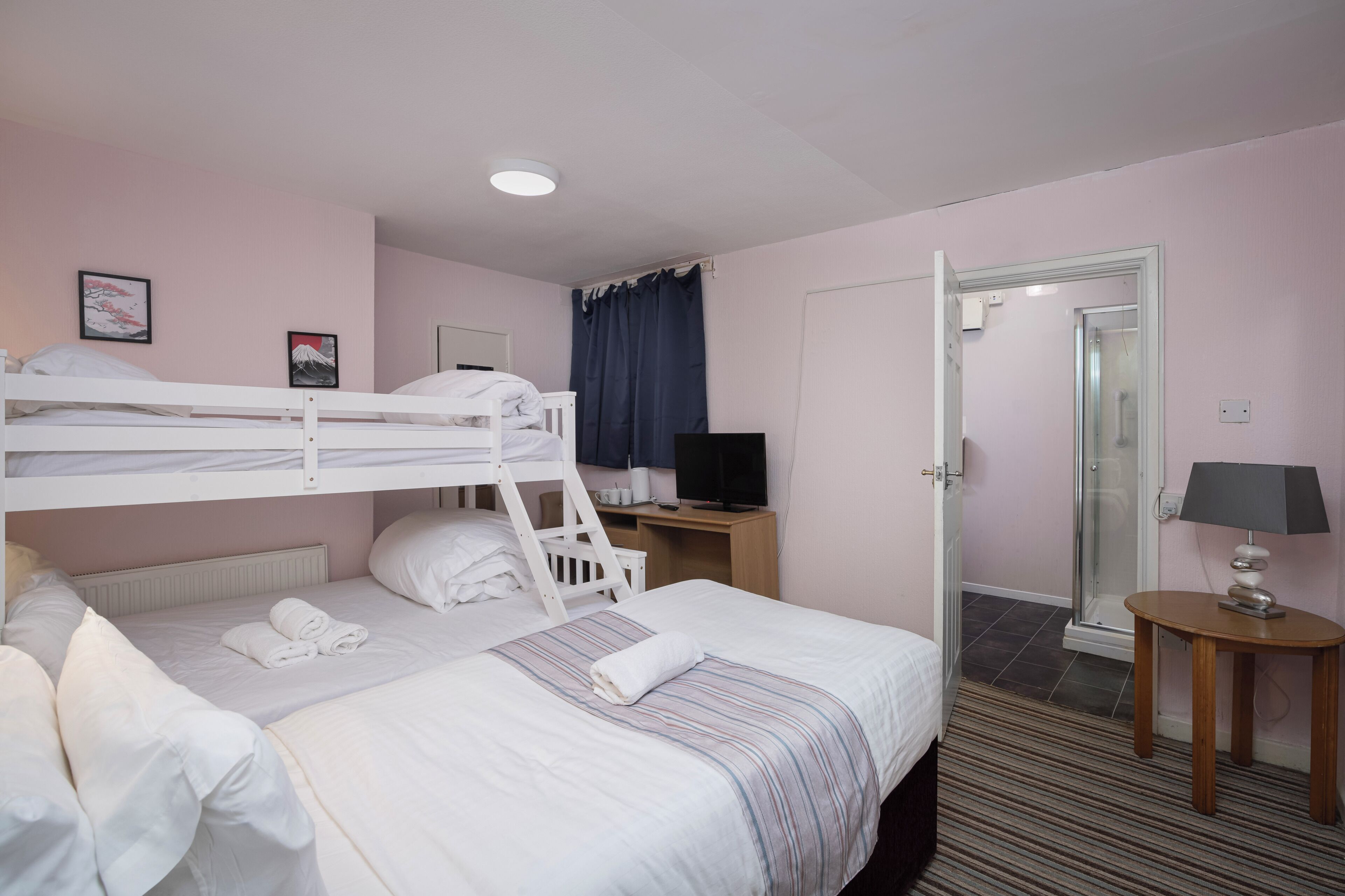 A hotel room with bunk beds, a television, a desk, a lamp, and a shower area.