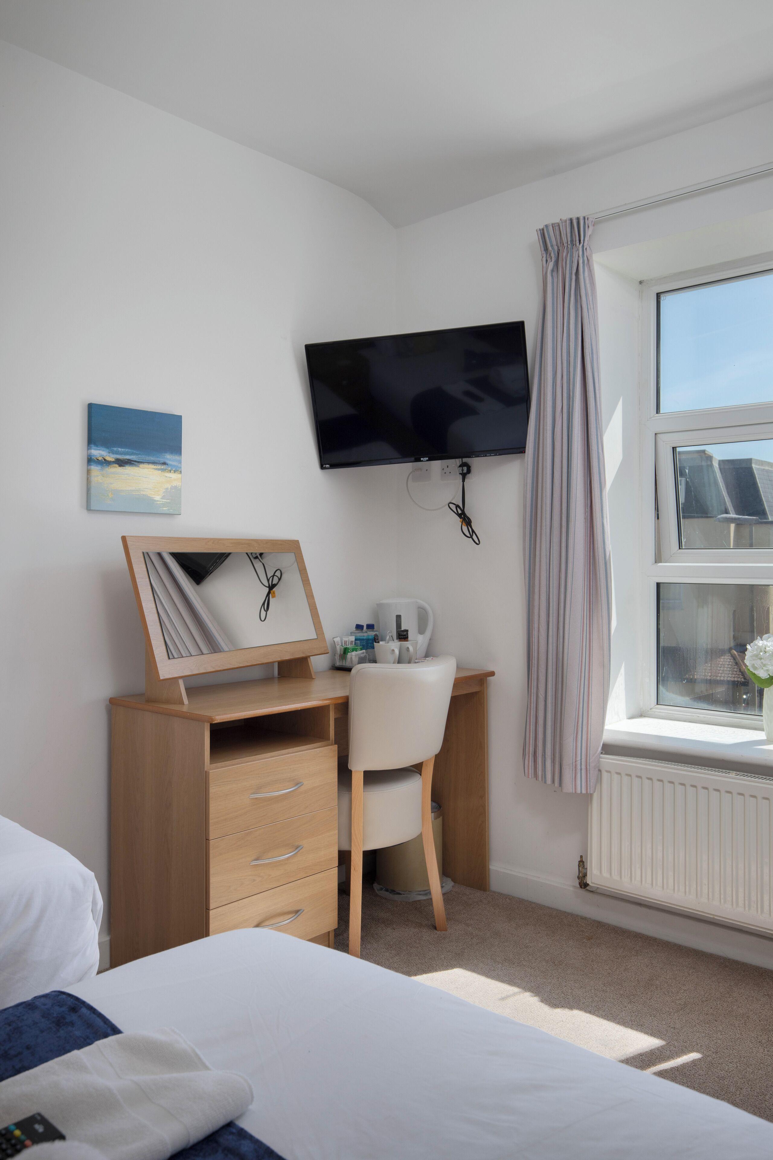 A hotel room with a bed, a desk with a chair, a television mounted on the wall, and a window with curtains.