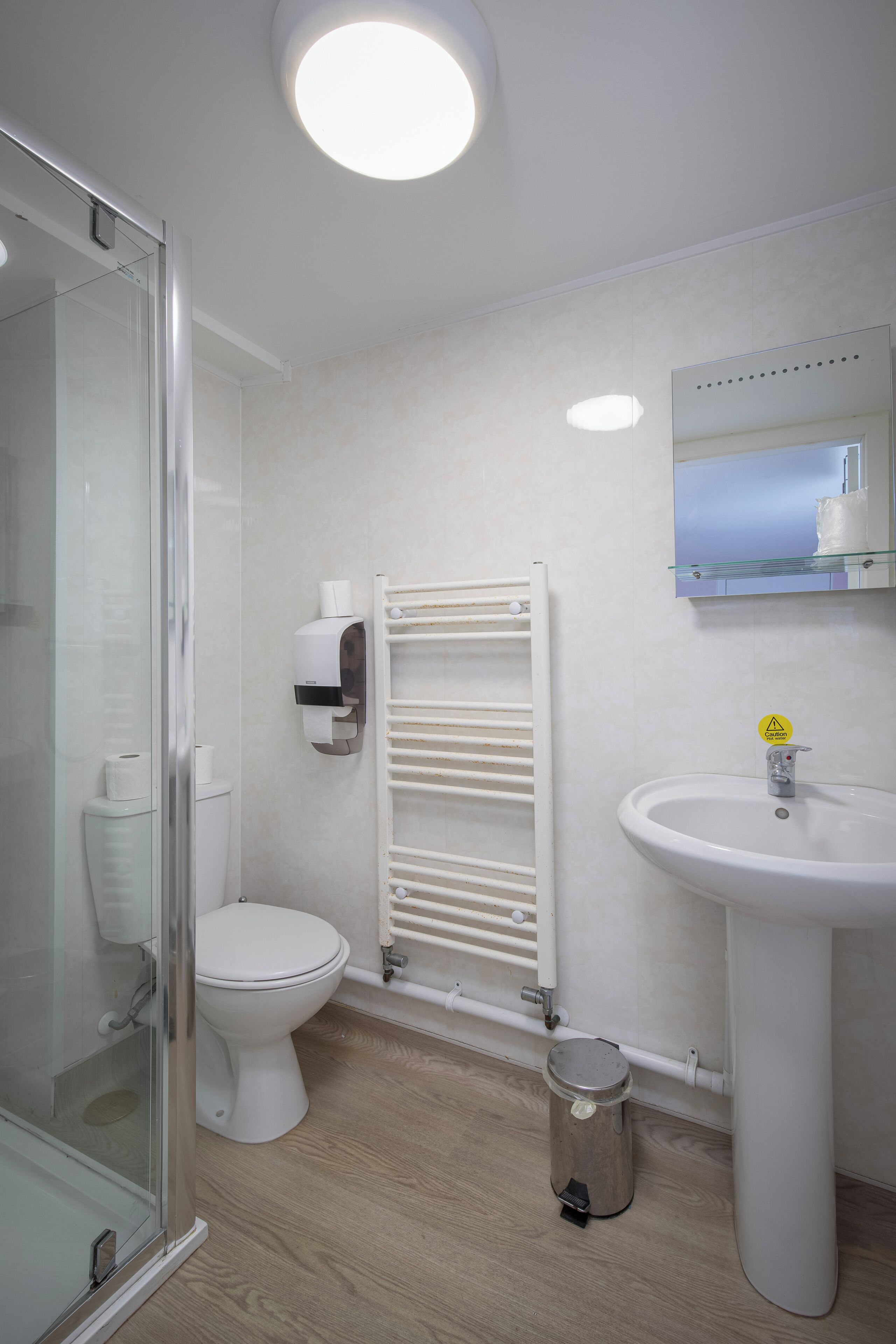 A bathroom with a glass shower enclosure, a toilet, a white sink, and a towel rack.