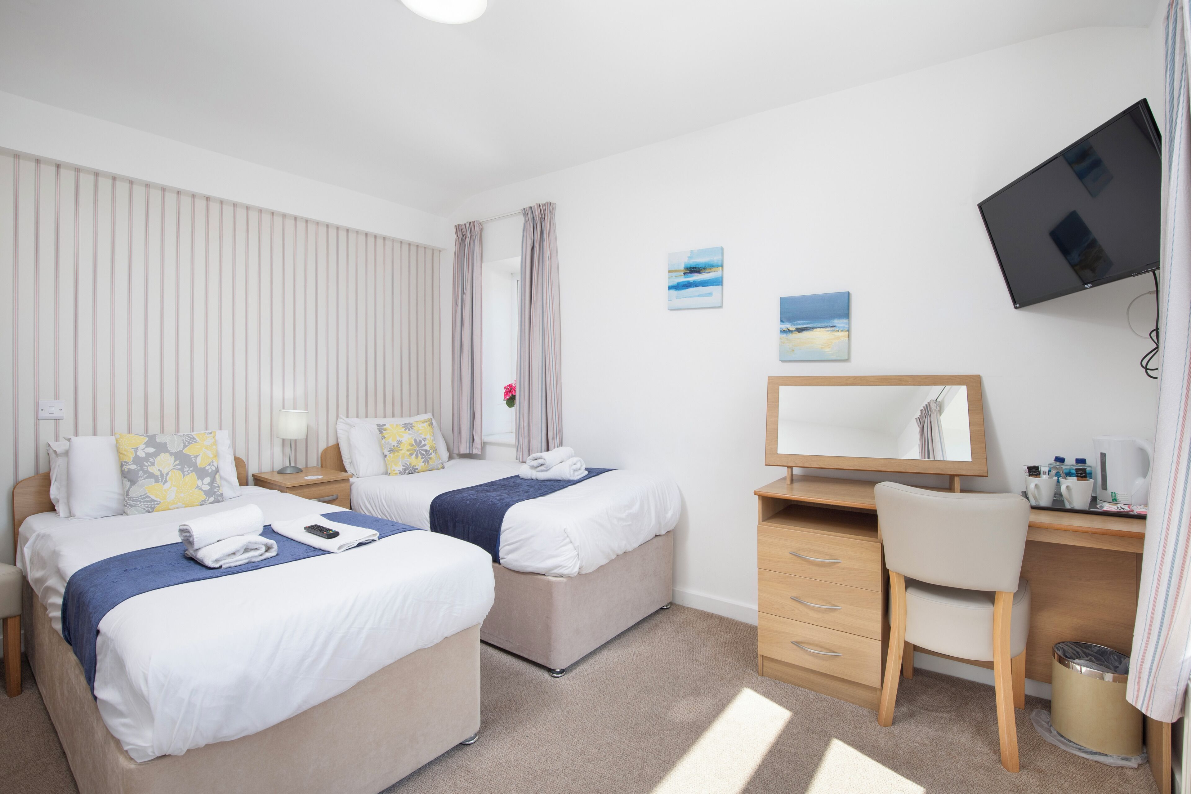 Une chambre d’hôtel avec deux lits, un bureau, une chaise, une télévision et une fenêtre avec des rideaux.
