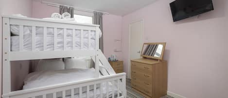 A bunk bed room with a TV, wooden dresser, and a mirror.