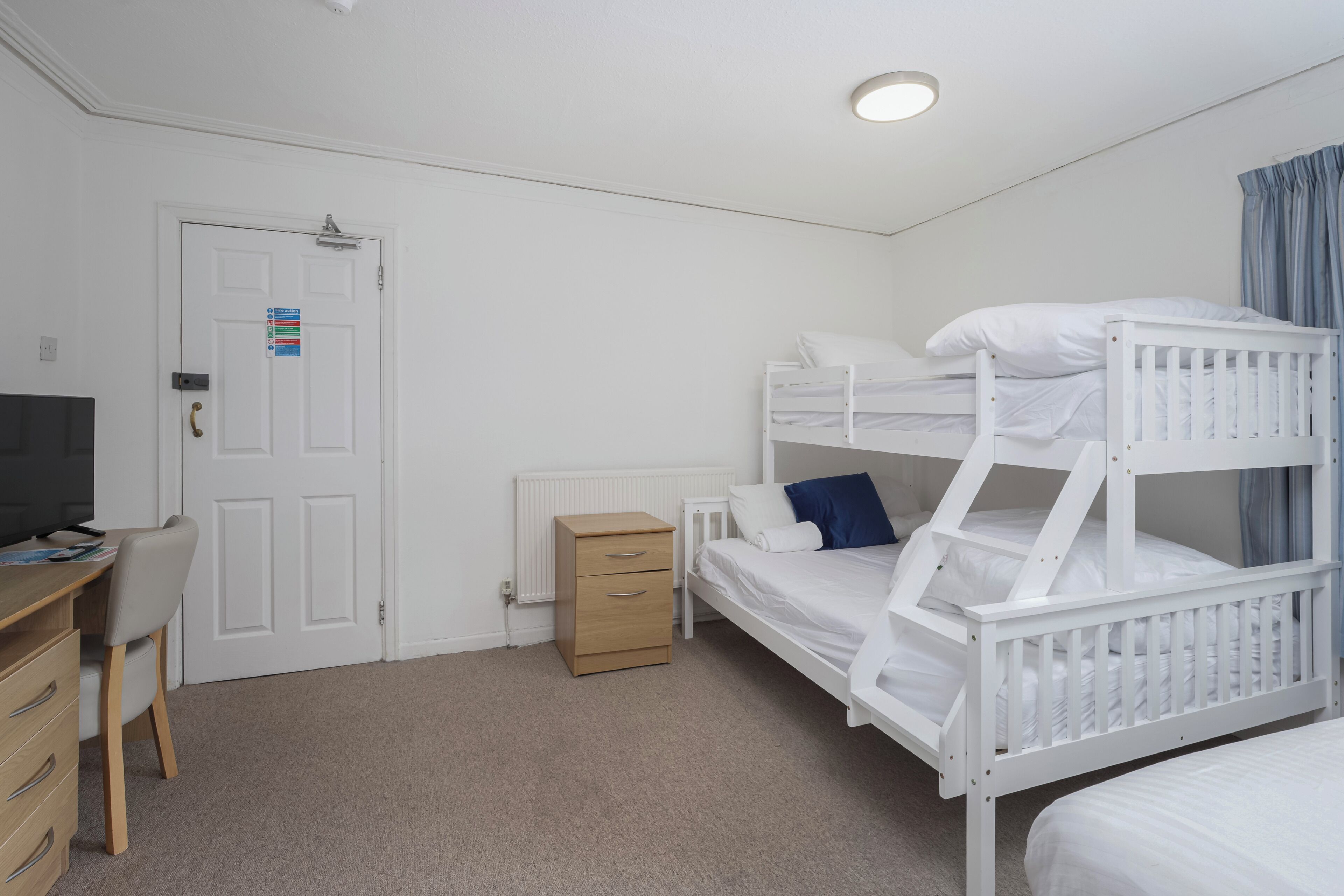 A bedroom with bunk beds, a desk, a chair, a dresser, and a television.