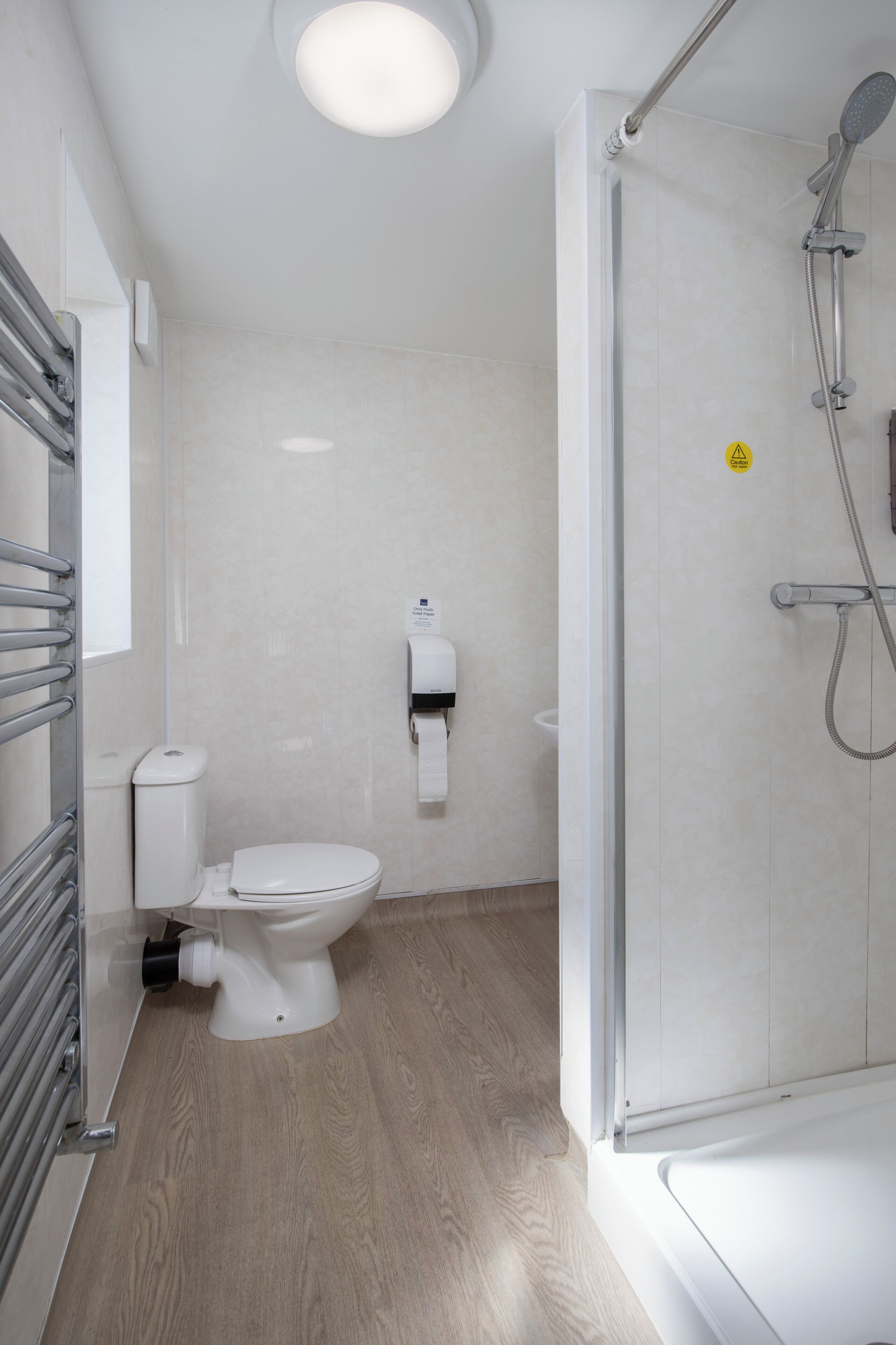 Een moderne badkamer met toilet, een papieren handdoekdispenser, een douchecabine met glazen wanden en een handdoekhouder.