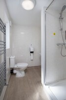 Een moderne badkamer met toilet, een papieren handdoekdispenser, een douchecabine met glazen wanden en een handdoekhouder.