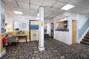 Een hotel receptie met een receptiebalie, een brandblusser, een kapstok en een bord met de hotelnaam.
