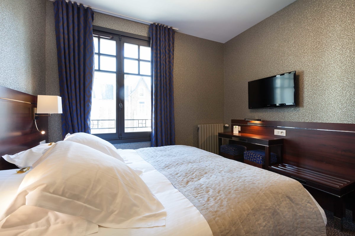 A hotel room with a large bed, a television mounted on the wall, and a window with curtains.