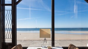Mesa com duas cadeiras e um candeeiro, virada para uma vista da praia através de grandes janelas.