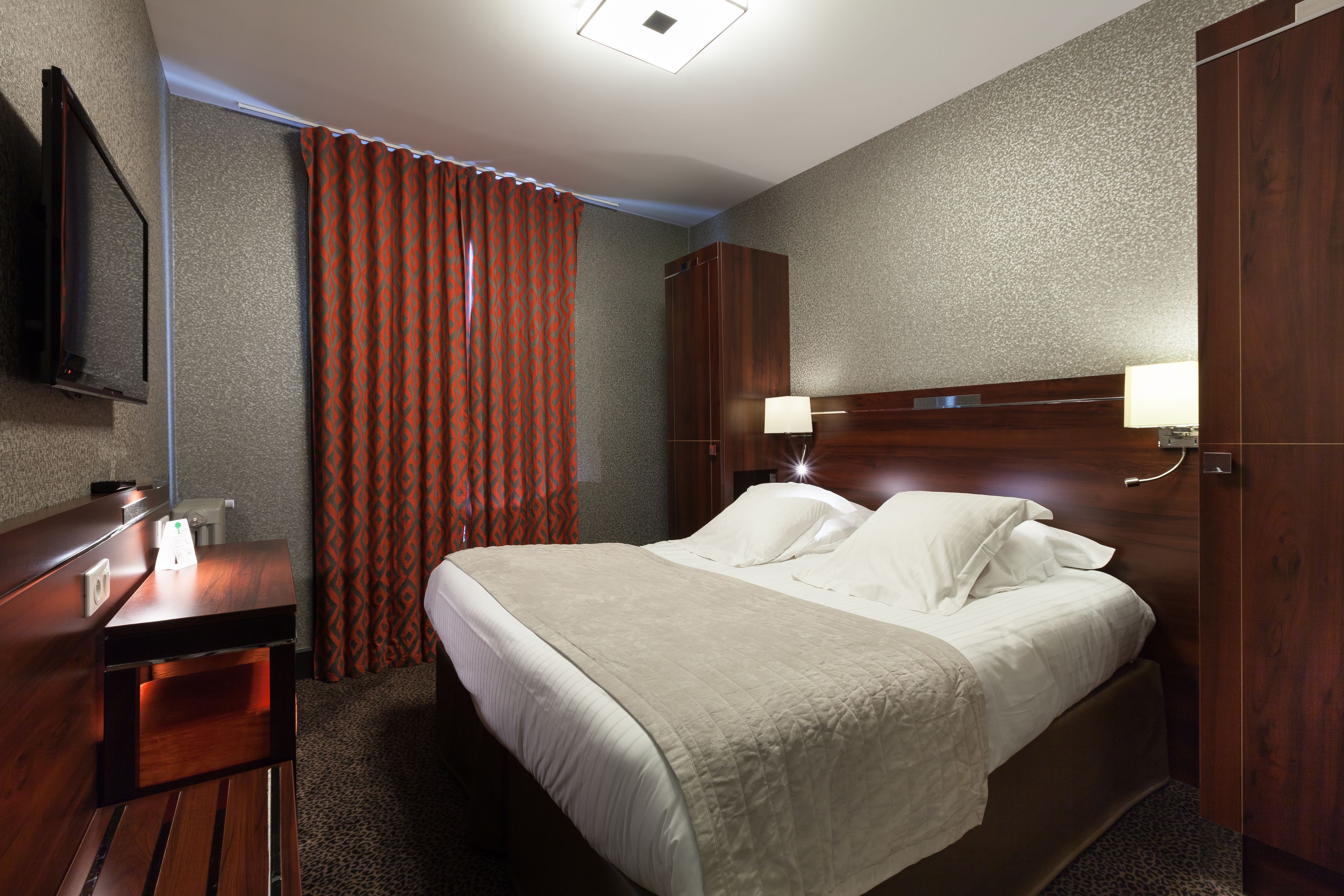 Une chambre d’hôtel avec un lit, des lampes de chevet, un bureau et un téléviseur.