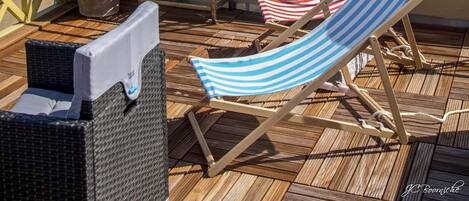 A deck with lounge chairs and a table overlooking a beach.