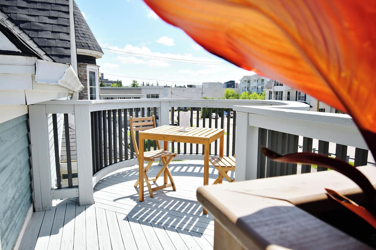 Een houten terras met een tafel en stoelen, een witte balustrade en een uitzicht op gebouwen op de achtergrond.