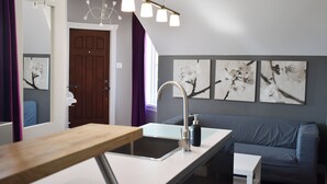 A modern bathroom with a wooden vanity, a sink, and a mirror. There is a blue sofa and a small table in the adjacent living area.
